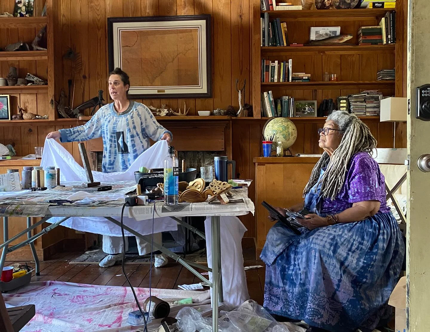 A textile workshop with cloth, dye supplies and carved printing blocks on a shared table.